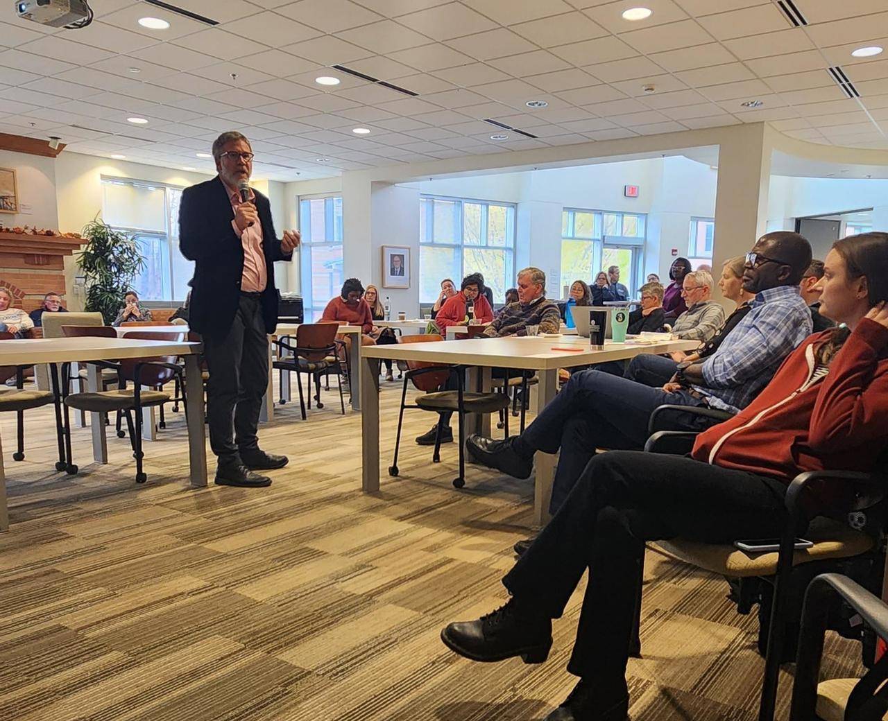 Dean Mark Schaub speaks into a microphone in front of a gathering of faculty and staff